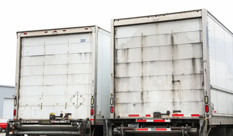Two dry van trailers side by side in a yard, one freshly washed and one not